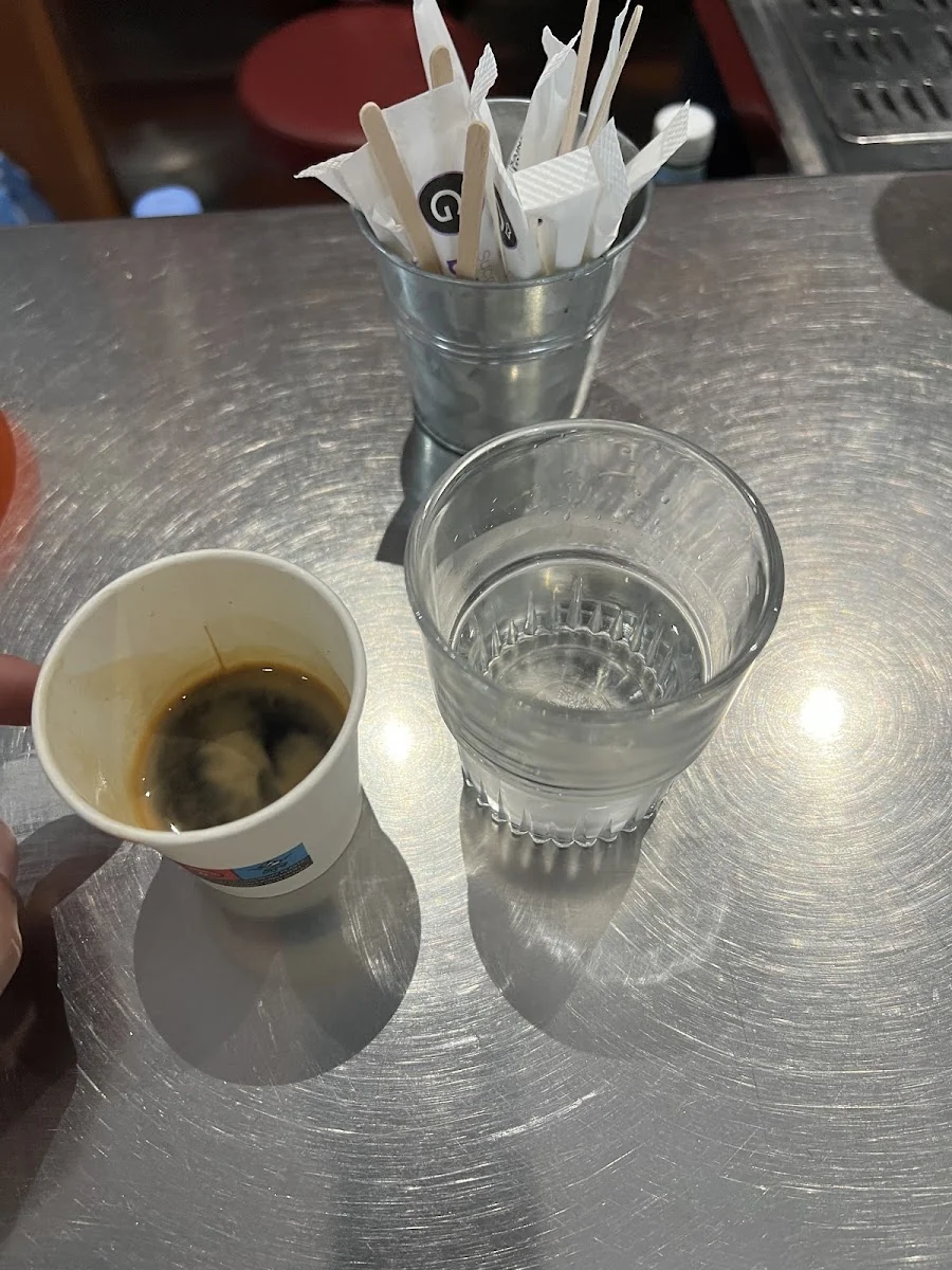 Un café express et un verre d'eau posés sur le comptoir en zinc, avec le pot à sucres