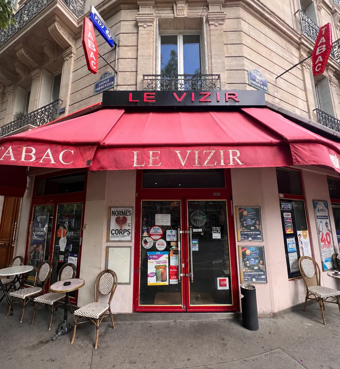 La façade du Vizir au 126 avenue Parmentier: store rouge portant LE VIZIR et TABAC, chaises en rotin et tables rondes sur le trottoir